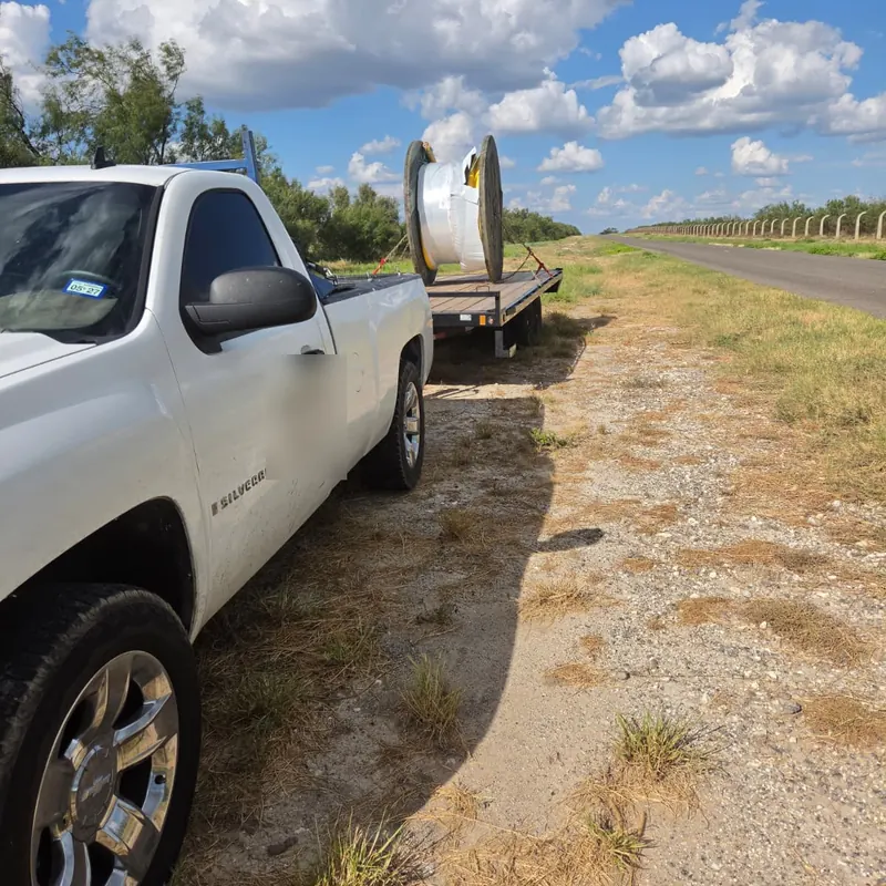Pickup truck hauling a cable reel on a hotshot flatbed trailer along a Texas highway